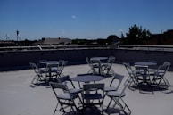 A bright and airy rooftop dining area featuring a round glass table and colorful chairs.