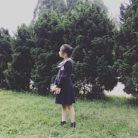A young girl proudly holding a schoolbook, standing on a pathway lined with trees.