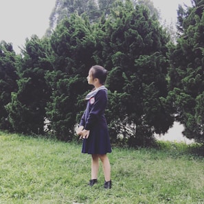 A young girl proudly holding a school book, standing outside her home.
