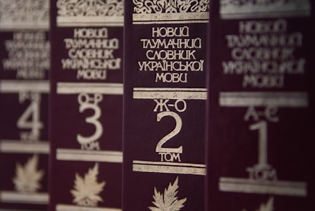 Several volumes of books with dark brown covers and gold embossed titles in Ukrainian, arranged in a row. Each book has a volume number prominently displayed, and there are decorative designs and images of leaves on the covers.