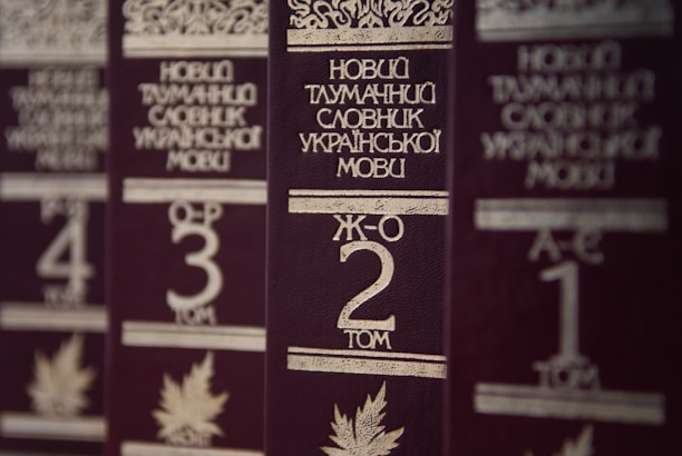 Several volumes of books with dark brown covers and gold embossed titles in Ukrainian, arranged in a row. Each book has a volume number prominently displayed, and there are decorative designs and images of leaves on the covers.