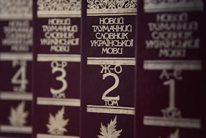 Several volumes of books with dark brown covers and gold embossed titles in Ukrainian, arranged in a row. Each book has a volume number prominently displayed, and there are decorative designs and images of leaves on the covers.