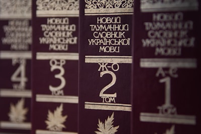 Several volumes of books with dark brown covers and gold embossed titles in Ukrainian, arranged in a row. Each book has a volume number prominently displayed, and there are decorative designs and images of leaves on the covers.