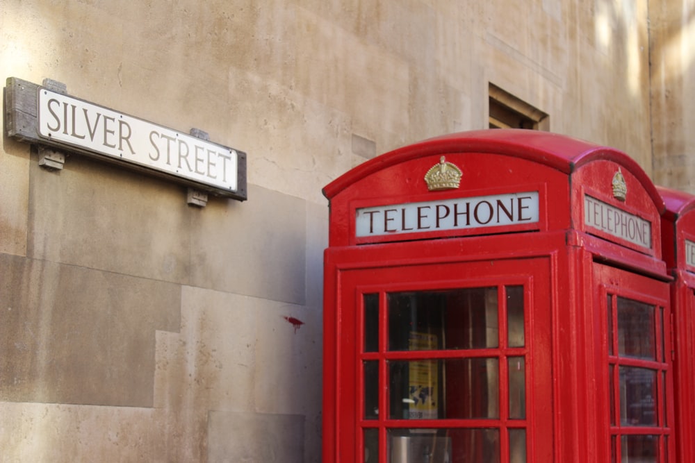 red telephone booth beside gray concrete building