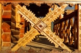 Intricate wooden carvings dominate the scene, featuring detailed geometric patterns and rich textures. The structure appears to be a decorative railing or architectural element, showcasing craftsmanship with various shades of wood.