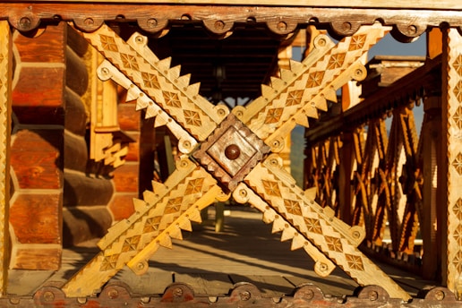 Intricate wooden carvings dominate the scene, featuring detailed geometric patterns and rich textures. The structure appears to be a decorative railing or architectural element, showcasing craftsmanship with various shades of wood.