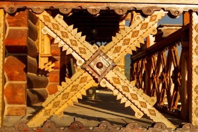 Intricate wooden carvings dominate the scene, featuring detailed geometric patterns and rich textures. The structure appears to be a decorative railing or architectural element, showcasing craftsmanship with various shades of wood.