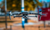 A vibrant close-up of an Aervox FPV drone hovering gently over a sunlit meadow, its bright colors catching the light.