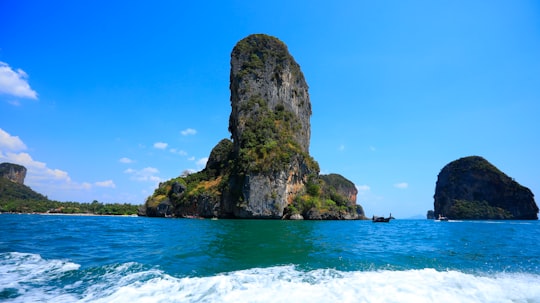 brown and green rock formation on sea under blue sky during daytime in Railay Beach Thailand