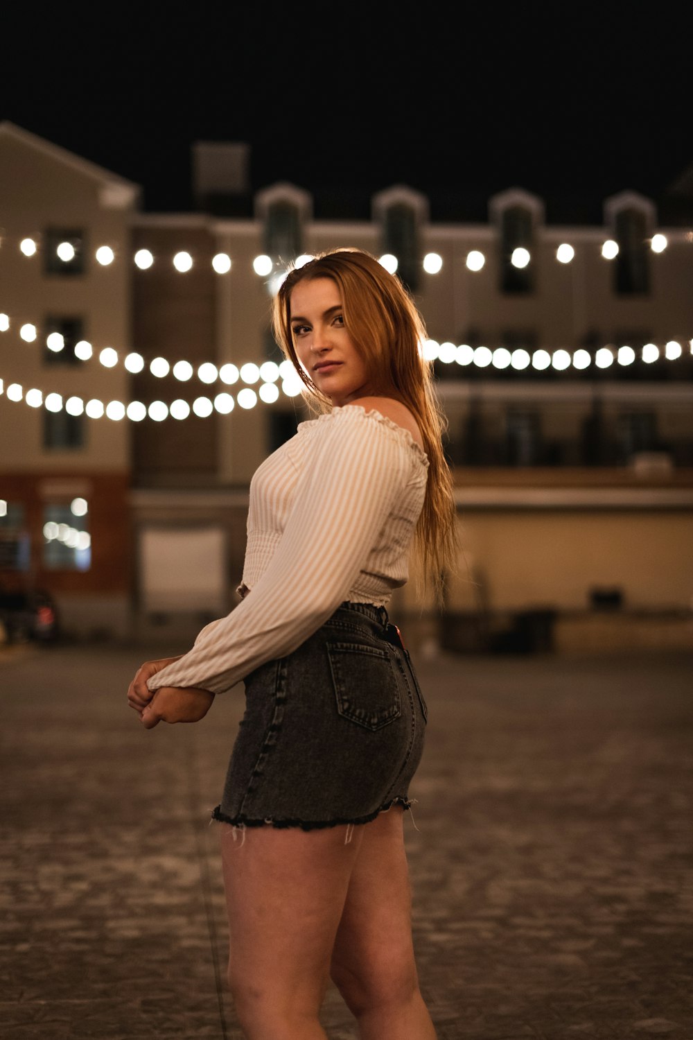 woman in white long sleeve shirt and black skirt standing on street during night time
