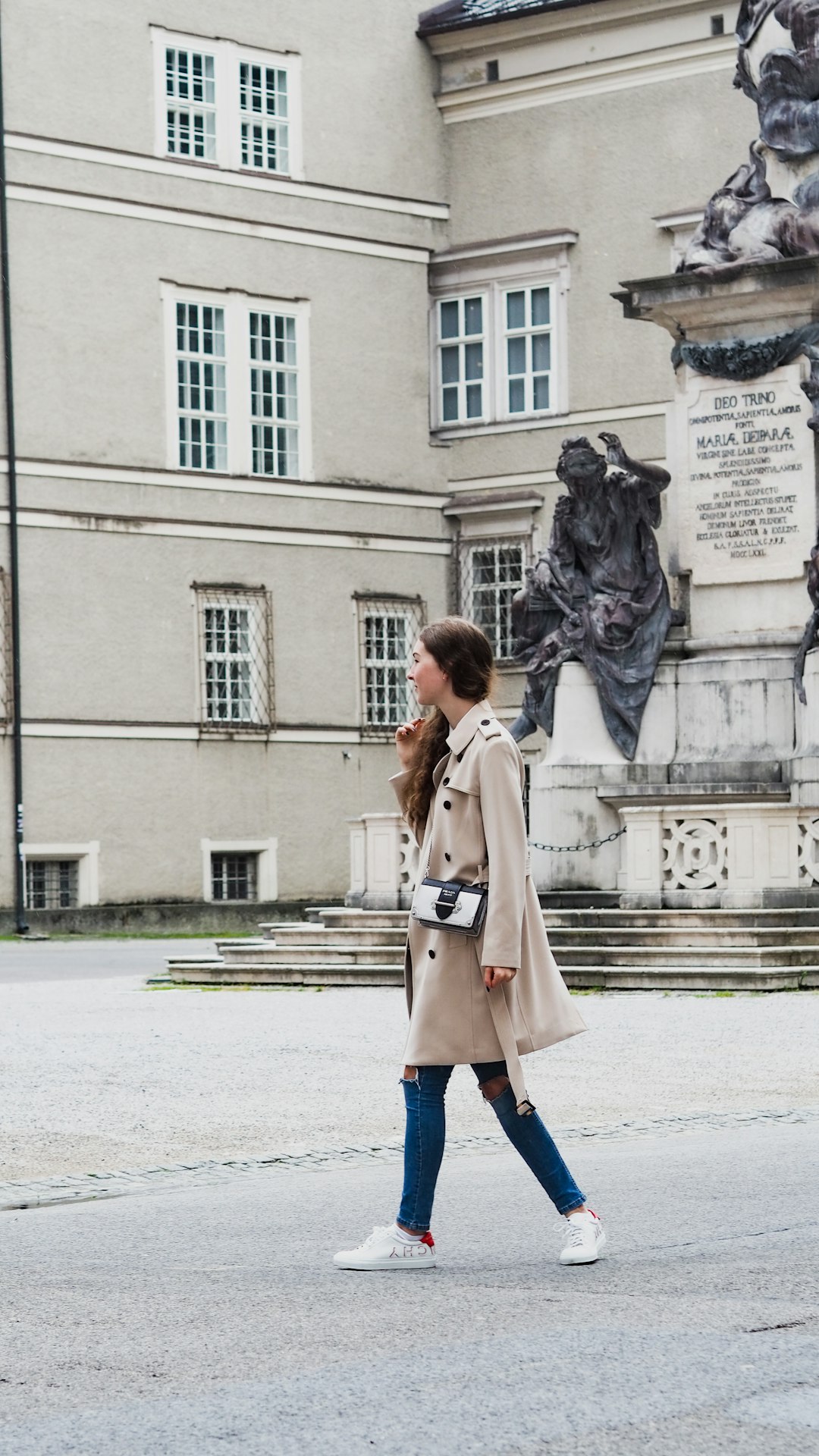 woman in brown coat standing near statue of man