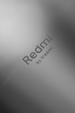 A close-up of a metallic or matte surface featuring the embossed text 'Redmi by Xiaomi' prominently.