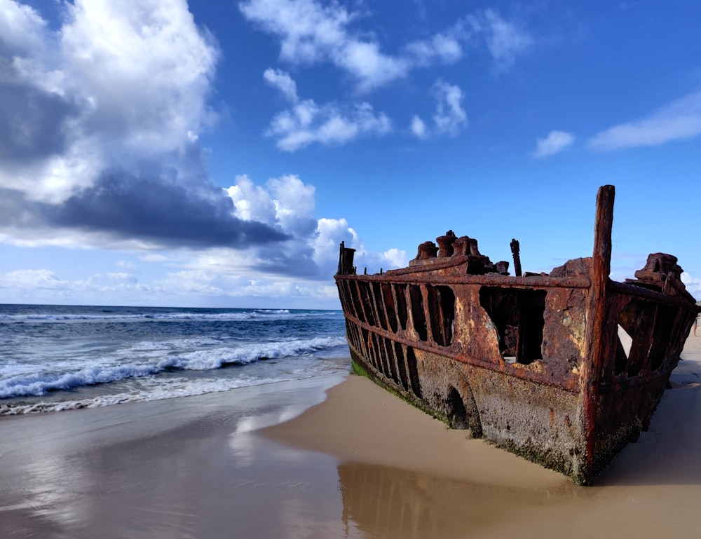 braunes Holzschiff am Meeresufer unter blauem Himmel und weißen Wolken tagsüber