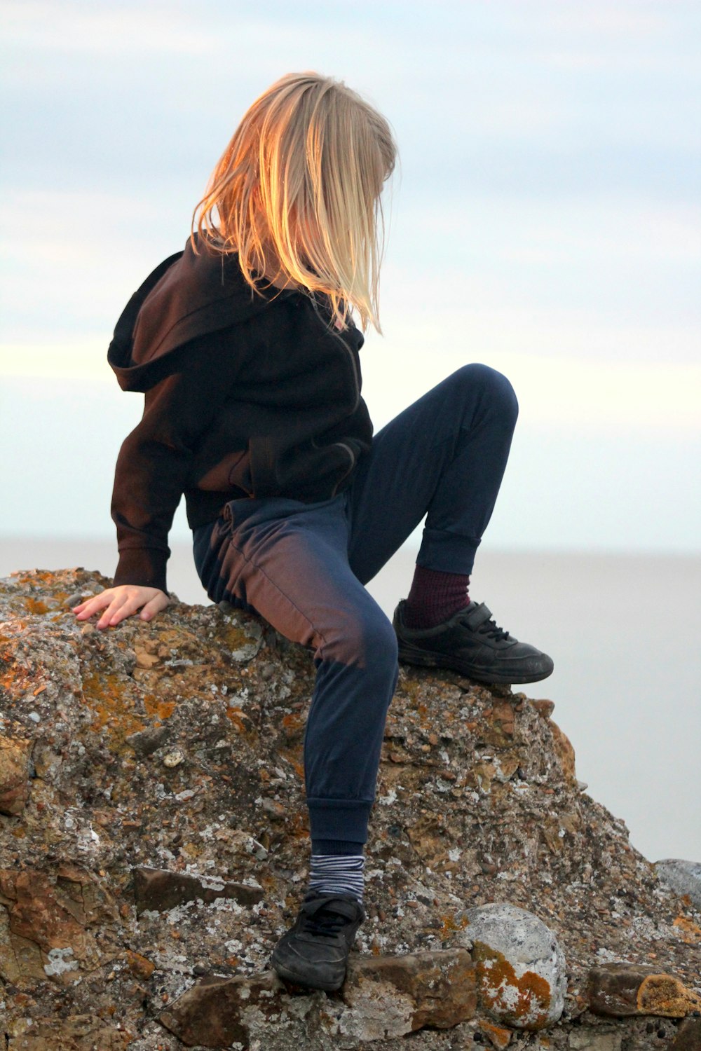 woman in black jacket and blue denim jeans sitting on rock