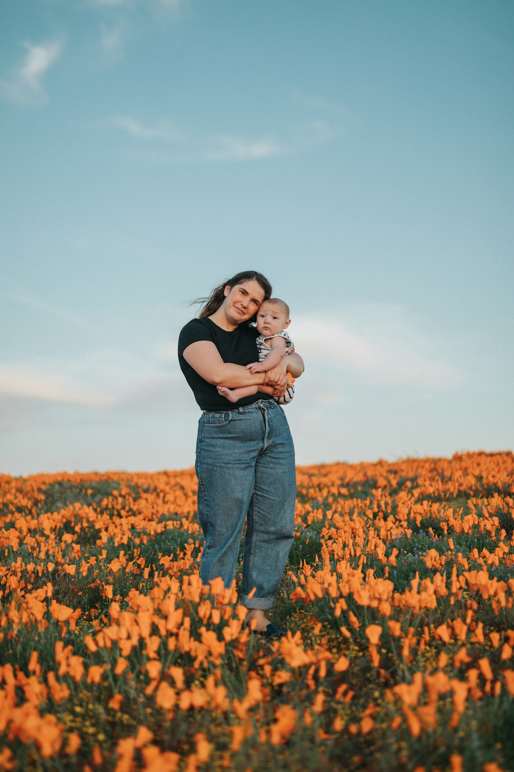 woman in black shirt and blue denim jeans carrying baby in black shirt on yellow flower