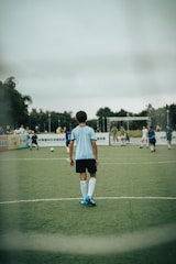 man in white and blue soccer jersey standing on green field during daytime
