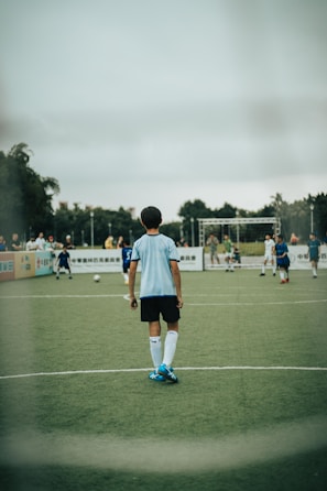 man in white and blue soccer jersey standing on green field during daytime