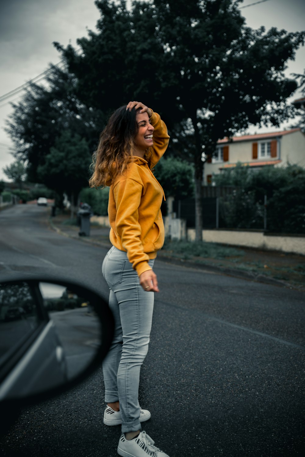 Mujer con sudadera con capucha amarilla y pantalones grises de pie en la carretera durante el día