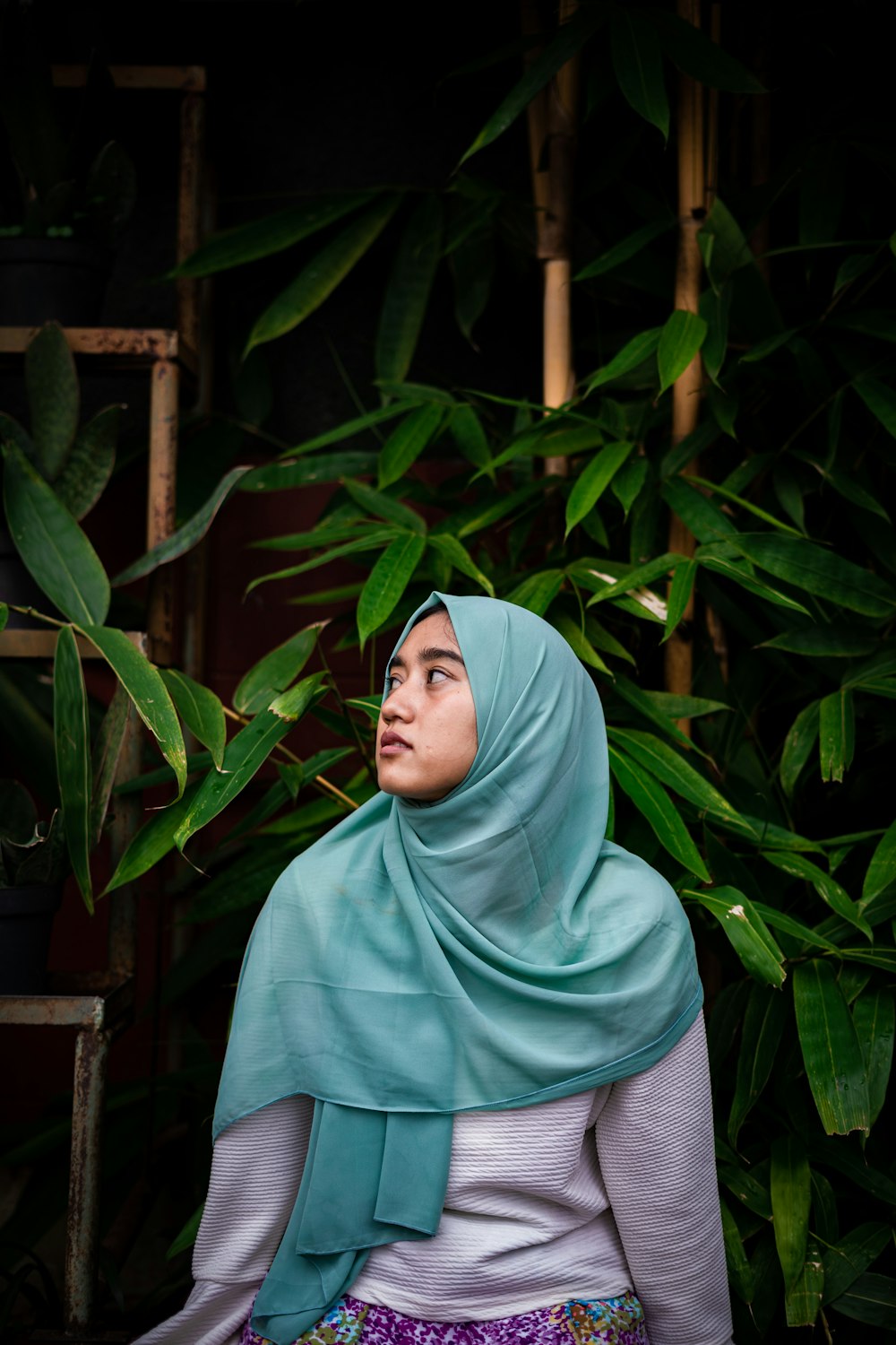 woman in teal hijab standing near green plants