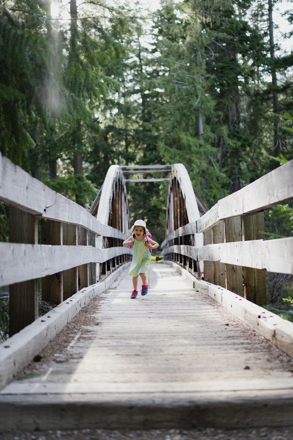 girl in green jacket walking on wooden bridge