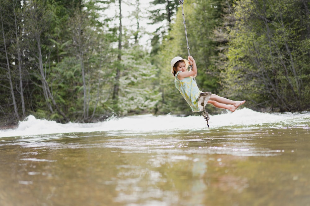 boy in green t-shirt and brown shorts riding on swing over river during daytime