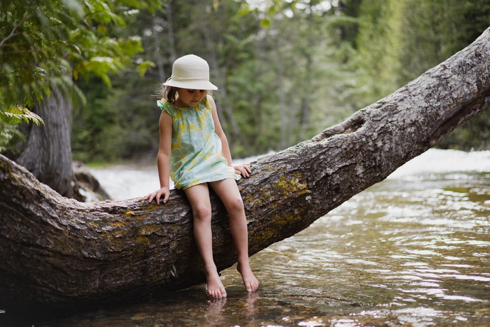 girl in green shirt and brown hat sitting on tree log in river during daytime