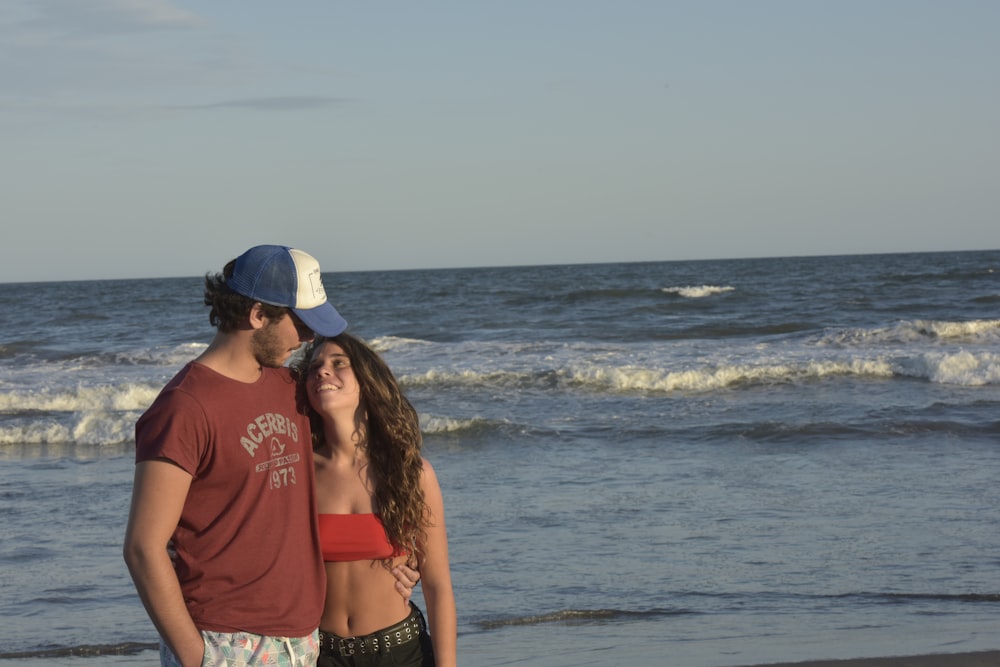 Donna in camicia rossa e denim blu Daisy Dukes in piedi sulla spiaggia durante il giorno