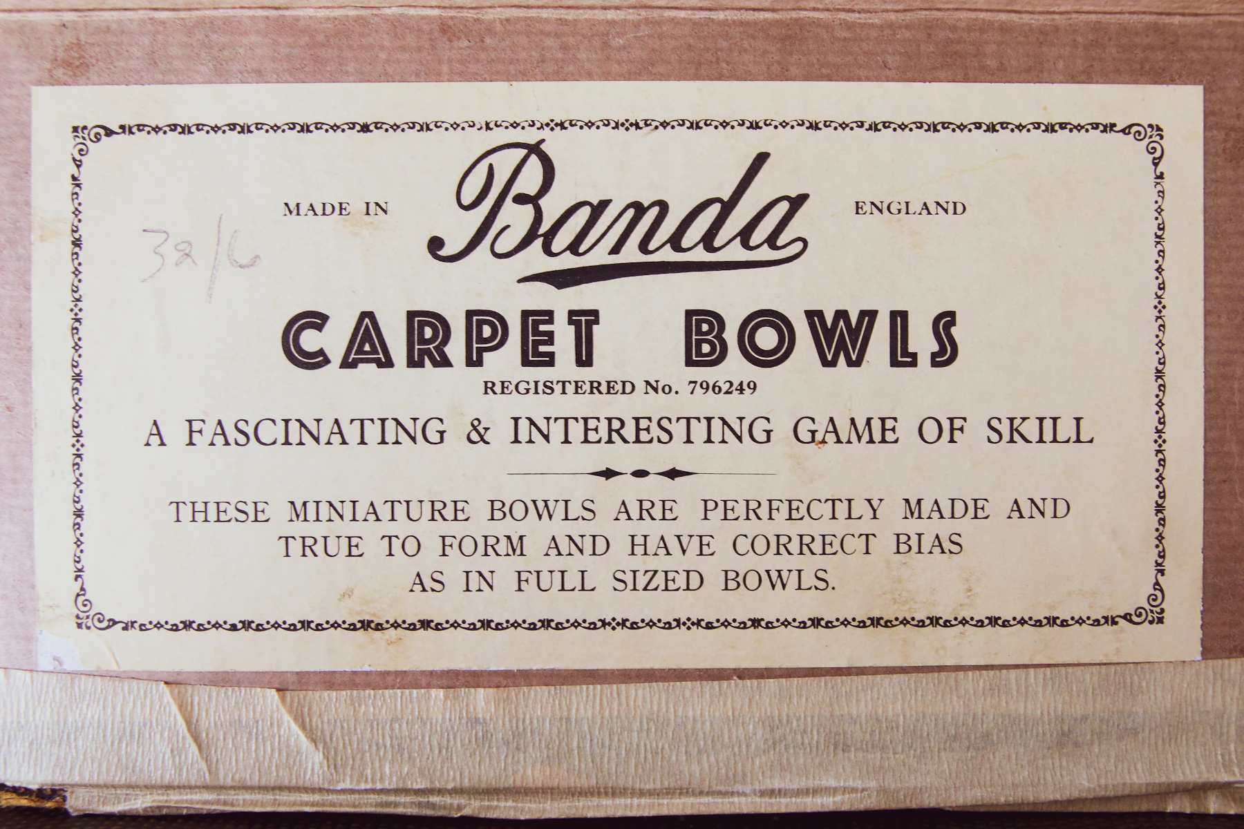 A cream printed label for a carpet bowls game pasted on a worn cardboard box lid, with a penciled price in one corner