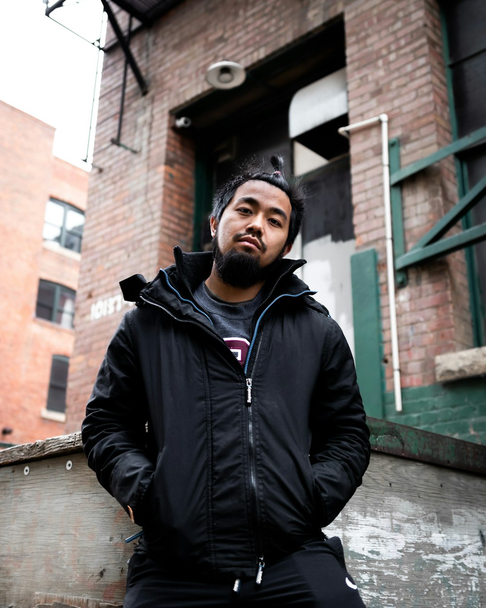 man in black zip up jacket standing beside brown brick building during daytime