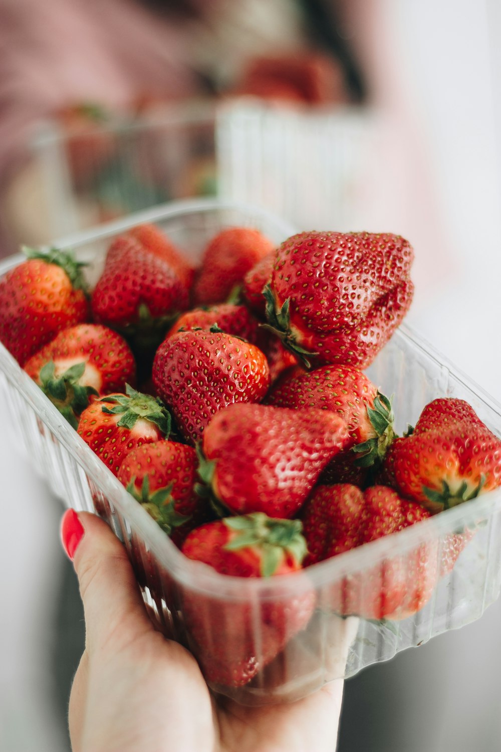 person holding red strawberries in plastic container