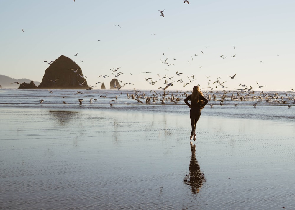 woman in black dress walking on beach during daytime