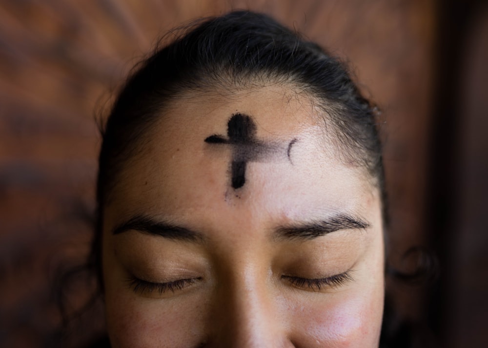 mulher com tatuagem de cruz preta em seu rosto