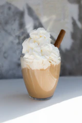 A creamy cappuccino topped with chocolate drizzle and a cinnamon stick.