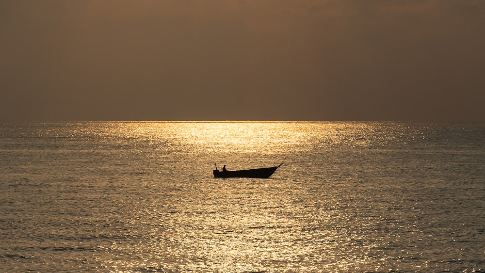 silhouette of person riding on boat on sea during sunset