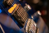 Close-up view of an electric guitar focusing on the strings, pickups, and controls with a warm, moody lighting.