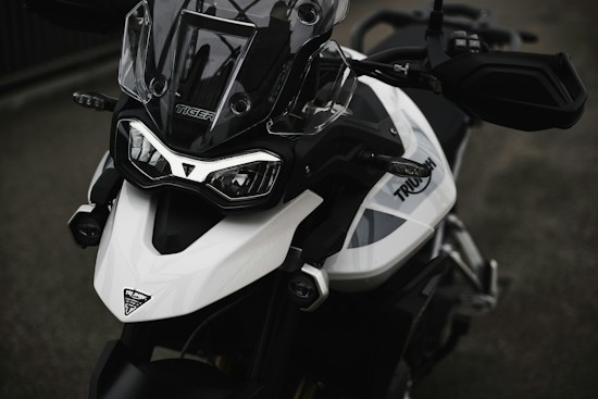 Close-up of a modern motorcycle with a prominent front design, featuring a black and white color scheme. The windshield is sleek and transparent, while the headlights are angular and aggressive. The motorcycle branding is visible on the side.