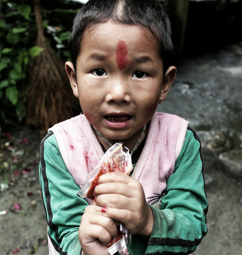 boy in green jacket holding red and white flower