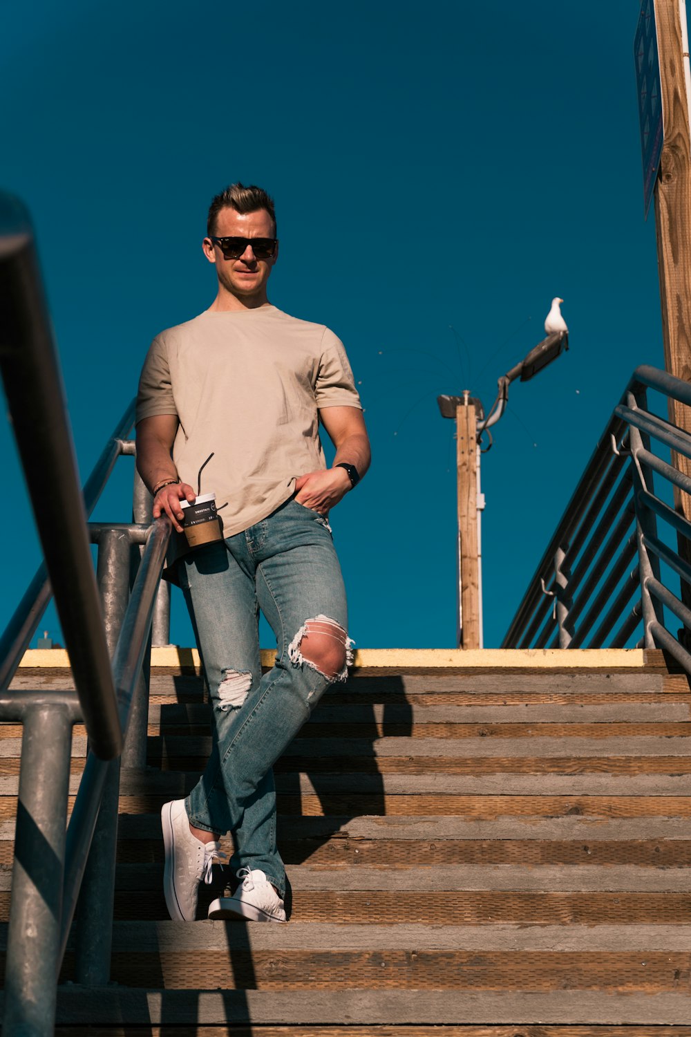 man in white long sleeve shirt and blue denim jeans standing on brown wooden bridge during