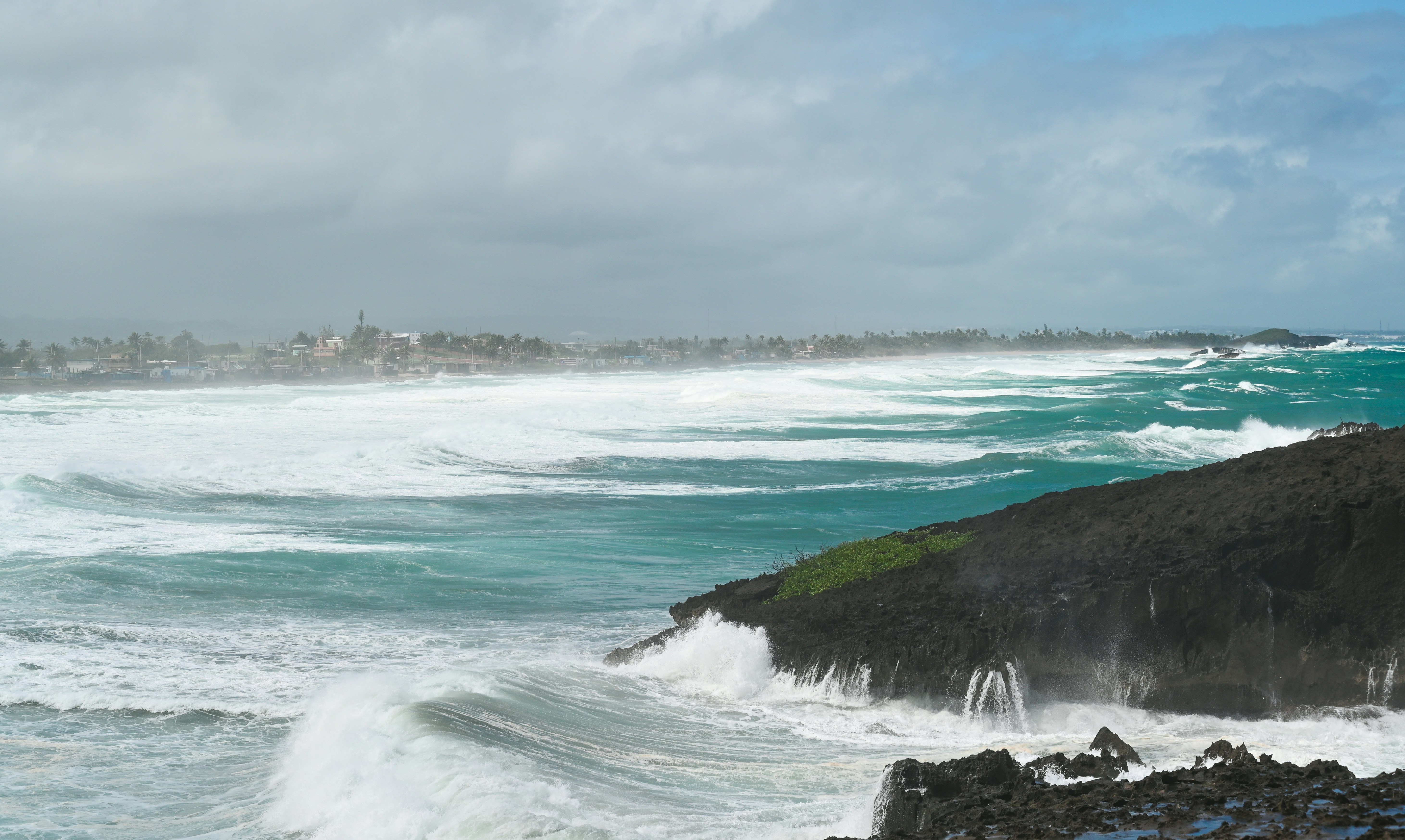 ocean waves crashing on rocks under white clouds during daytime