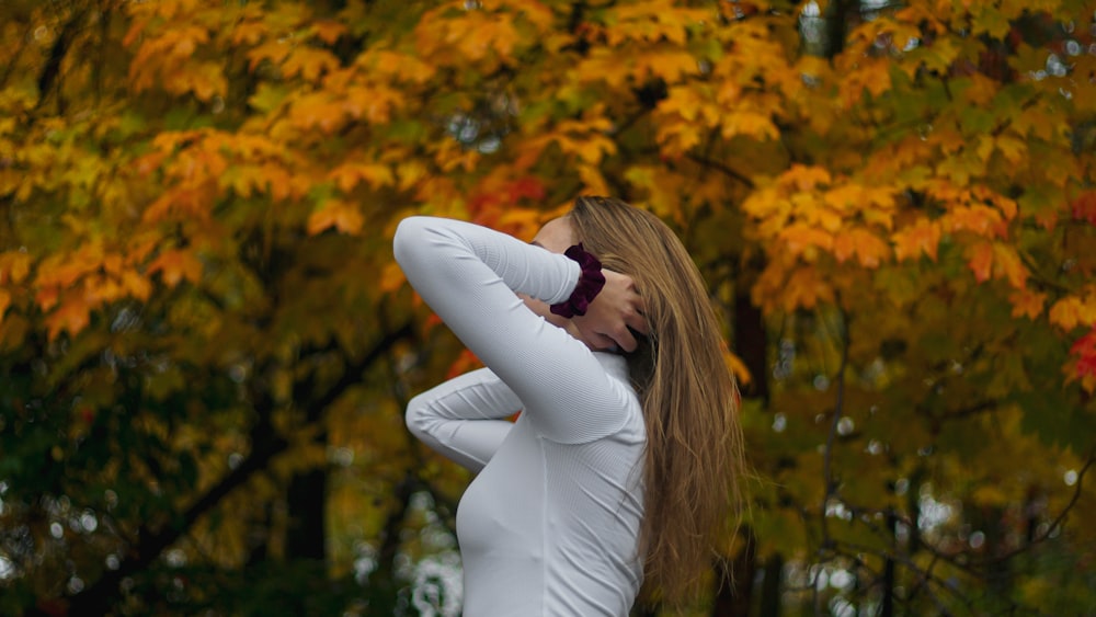 woman in white long sleeve shirt and white pants standing near yellow leaf trees during daytime