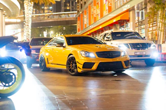 A bright yellow sports car gleaming under city lights at dusk.