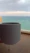 Close-up of a handmade ceramic cup with ocean waves painted on it, resting on a wooden table by the sea.
