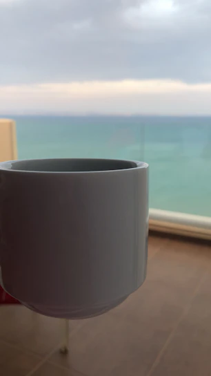 Close-up of a colorful UV printed mug featuring a coastal-inspired design in light blue and sand tones, filled with steaming coffee.