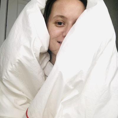 A person is wrapped warmly in a white comforter, with only their face partially visible. The expression appears relaxed and cozy.