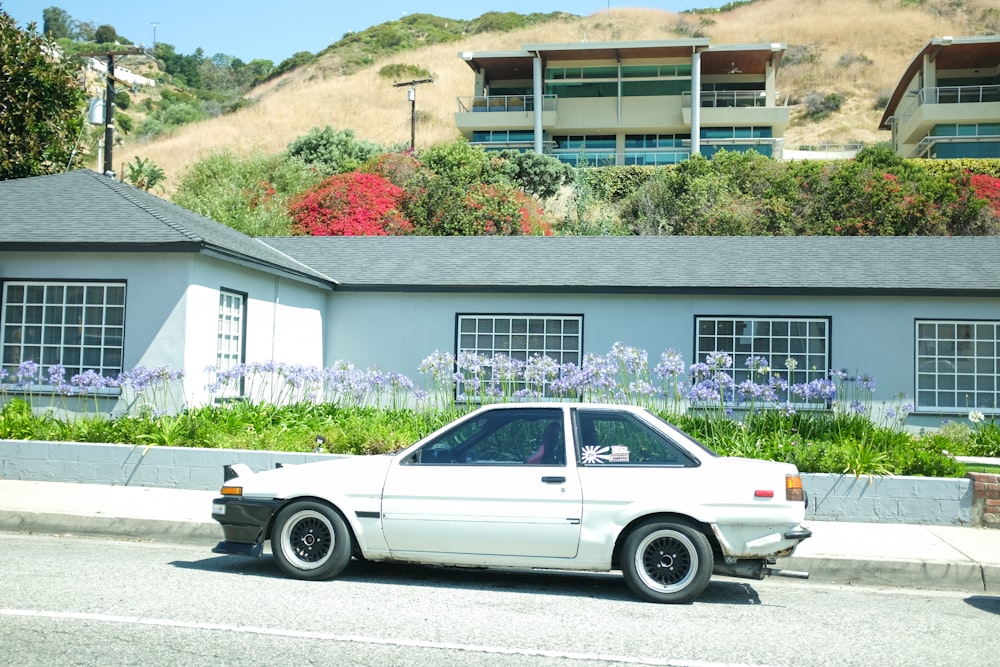 white sedan parked beside white and brown house during daytime