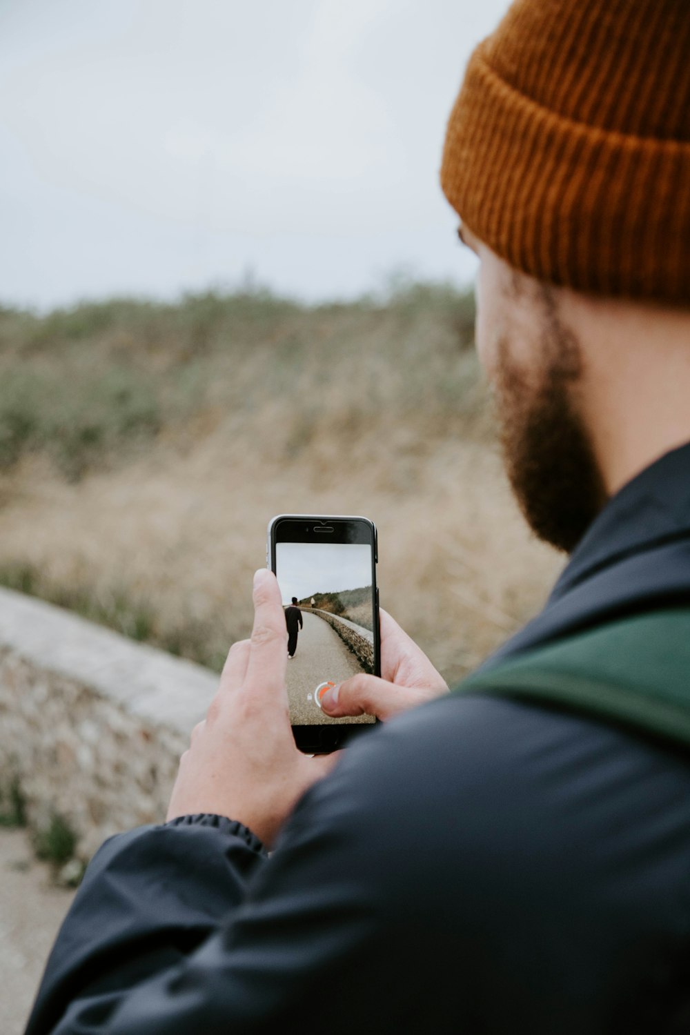 person in black jacket holding white smartphone taking photo of brown field during daytime