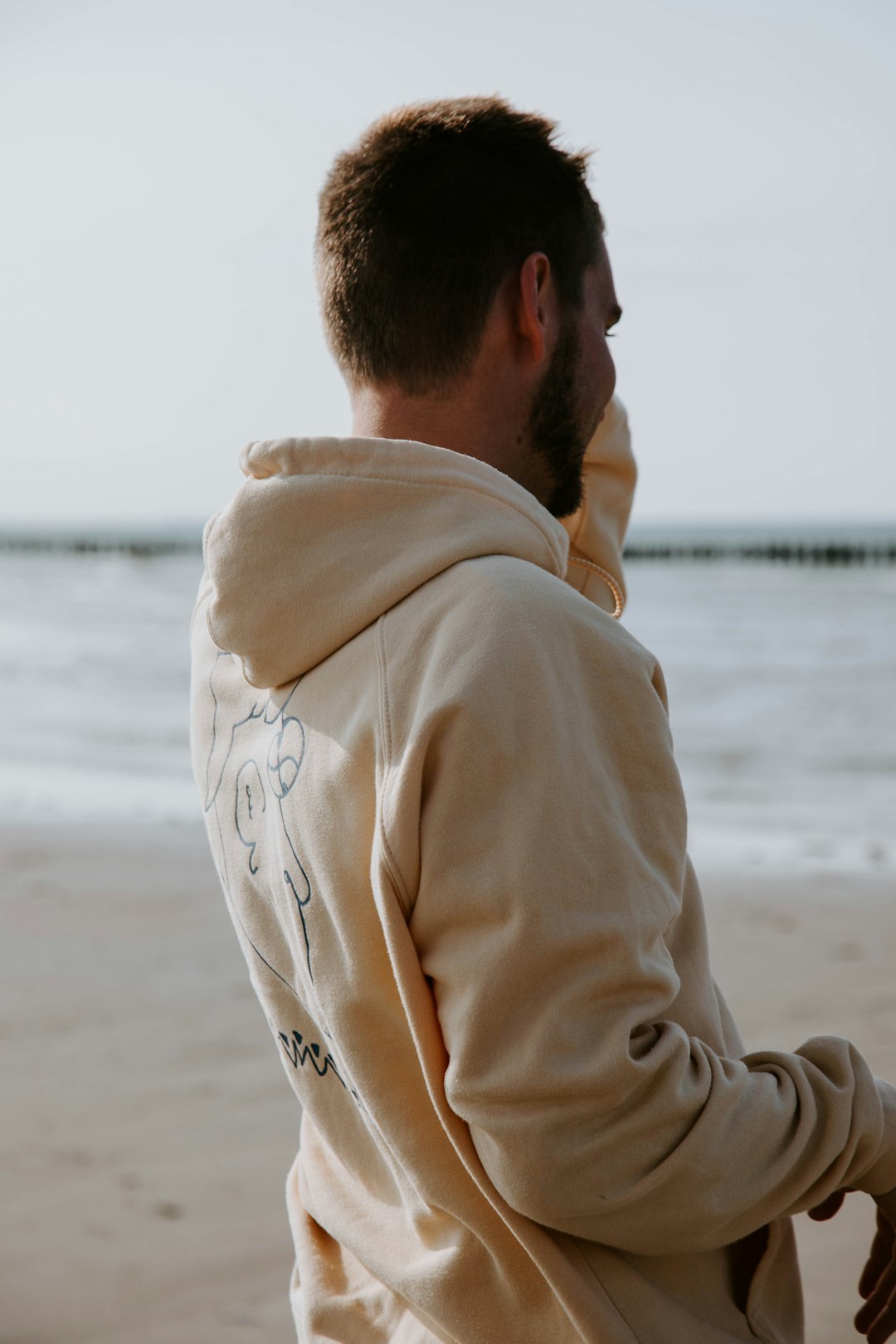 man in beige hoodie standing on beach during daytime