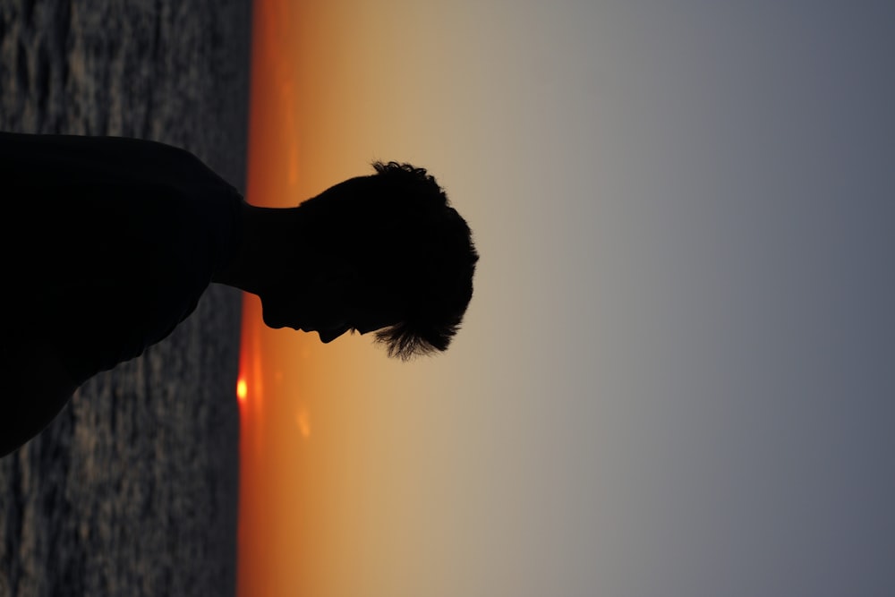 silhouette of man near body of water during sunset