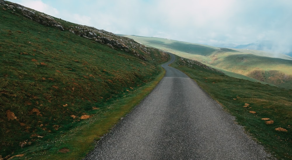 gray asphalt road between green grass field under cloudy sky during daytime