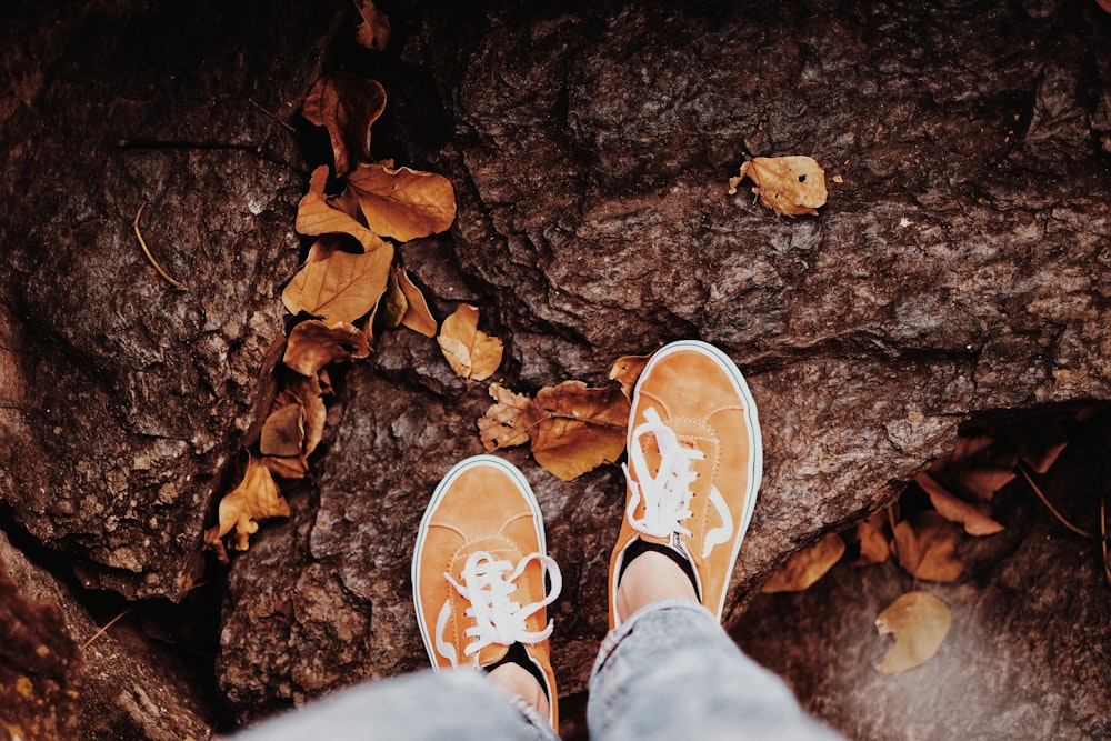 person in white pants and brown and white sneakers standing on dried leaves